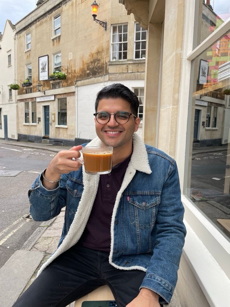Aakash Chugh smiling with a cup of coffee on a street in Bath