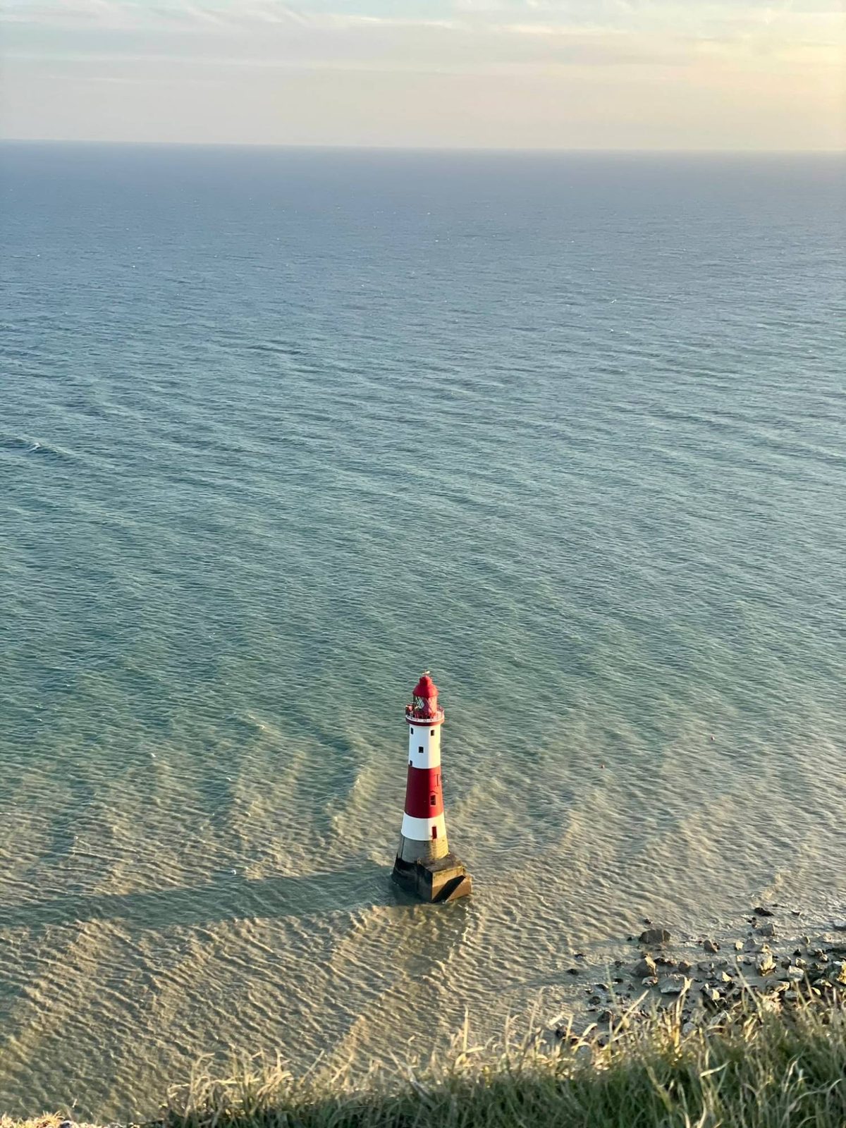 A red and white lighthouse in the sea below a chalk cliff