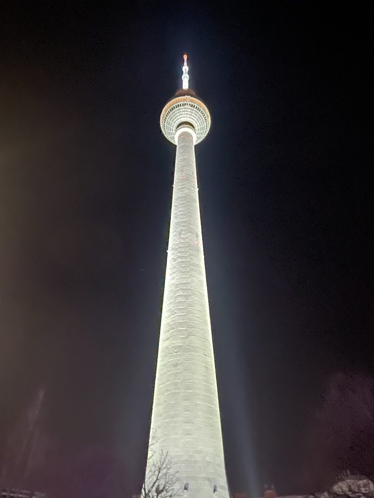 The Berlin TV tower lit white against a black night sky