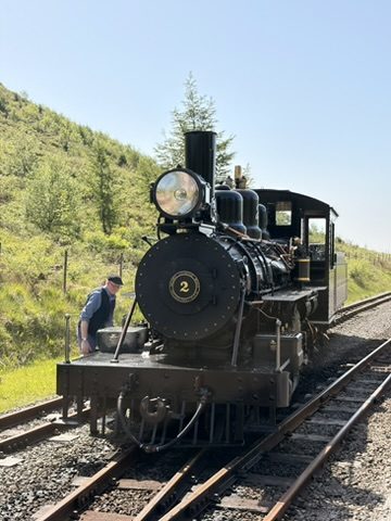 A black steam locomotive number 2 with a driver beside it on a hillside railway