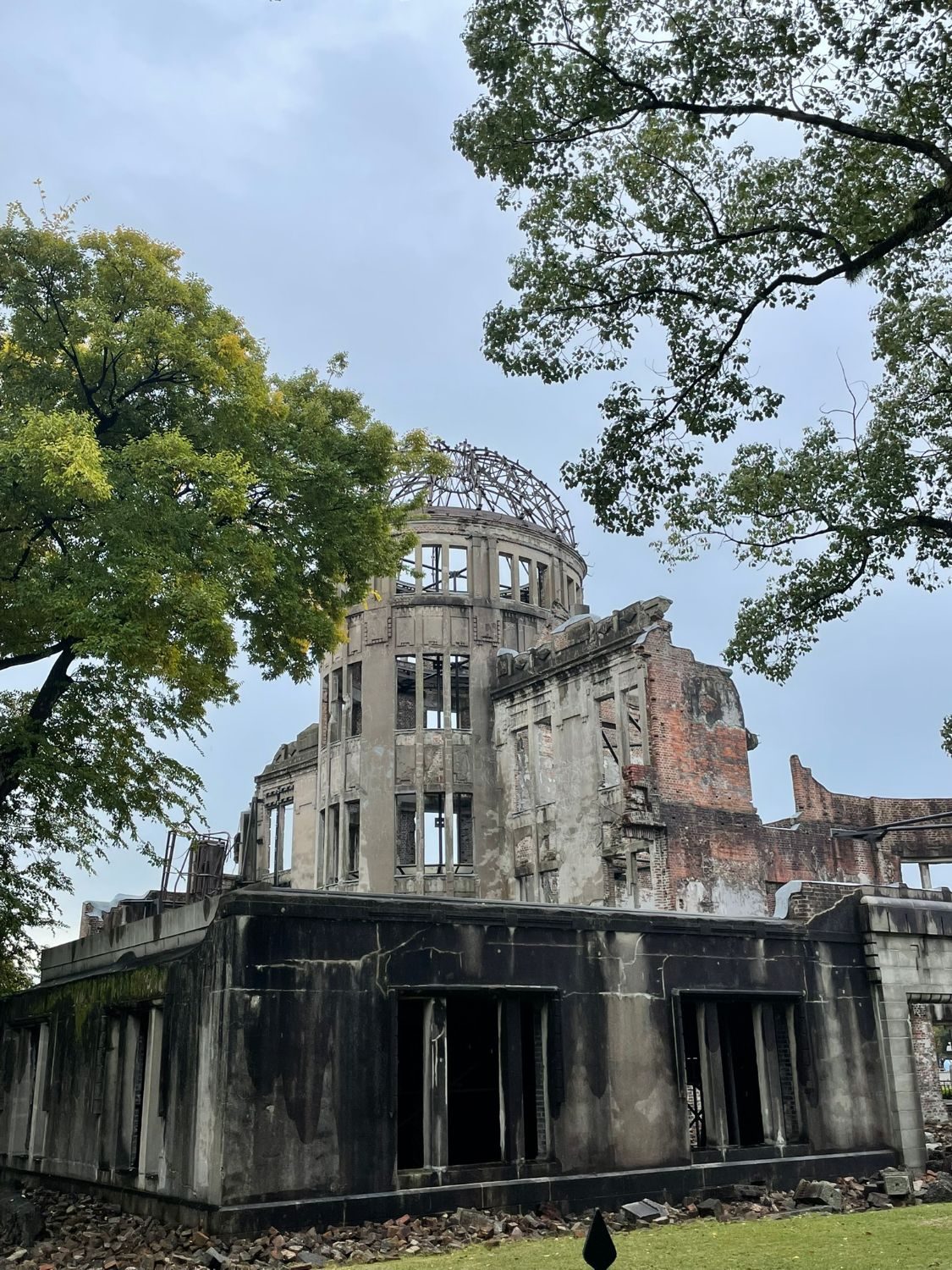 The ruined A-Bomb Dome in Hiroshima among trees under a grey sky