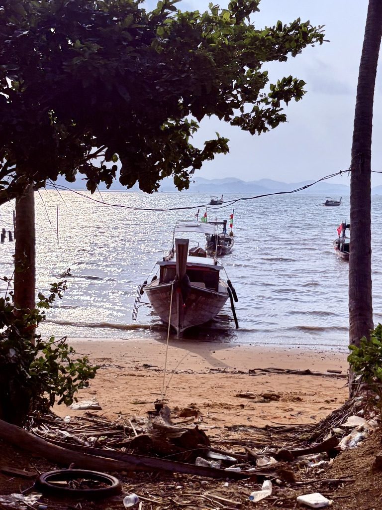 A longtail boat on the sand at Koh Yao Noi, framed by trees