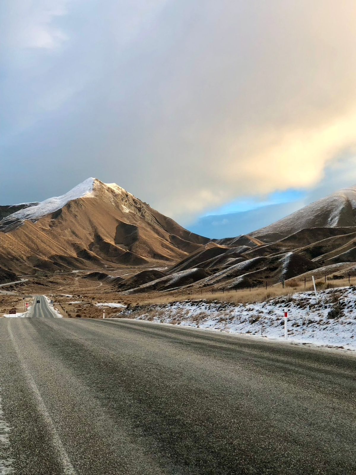 A road through snow-dusted tawny hills at Lindis Pass