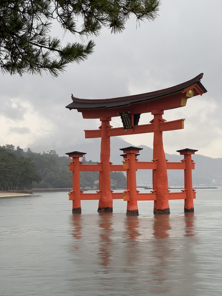 The red torii gate of Itsukushima Shrine standing in water on a misty day