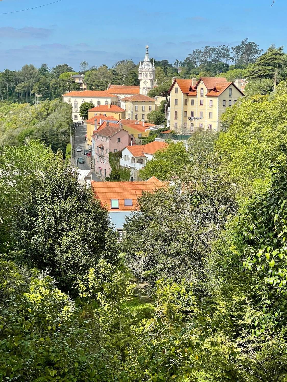 Terracotta roofs and a pointed clock tower among trees in Sintra
