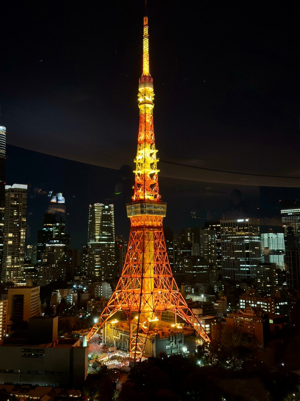 Tokyo Tower lit orange at night, seen through glass